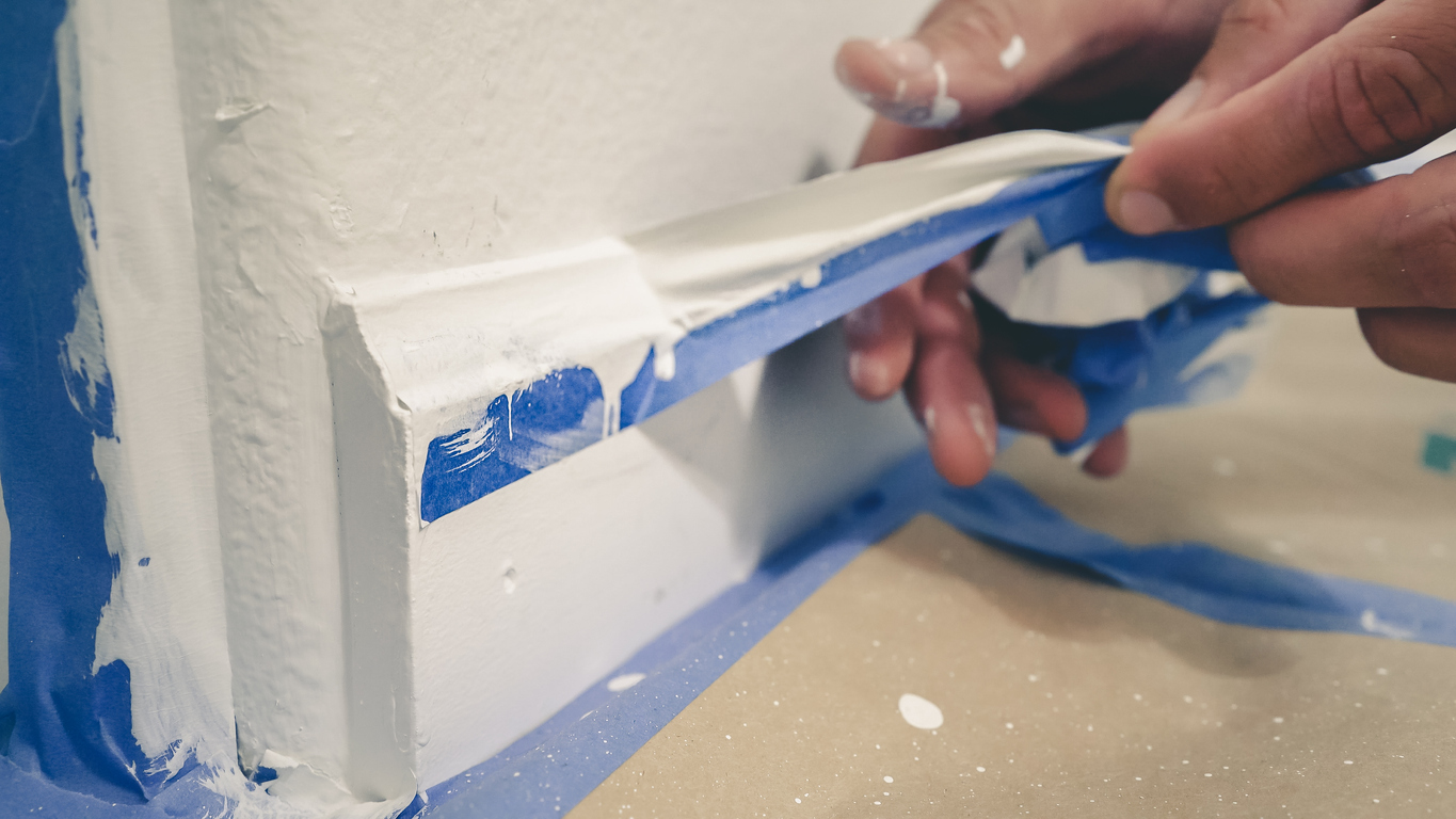 Removing masking tape from moulding. A painter pulls of blue painter's tape from the wall to reveal a clean edge baseboard.