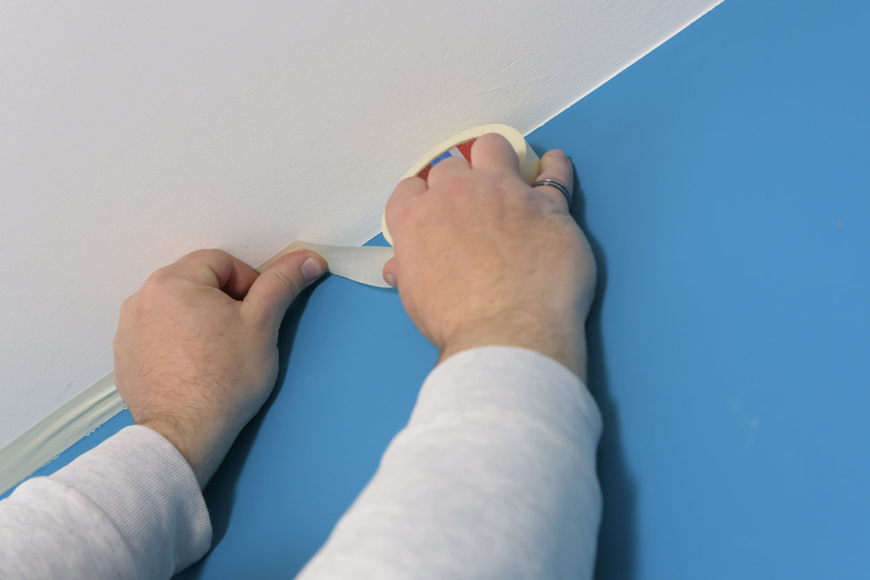 Applying masking tape between white ceiling and colored wall